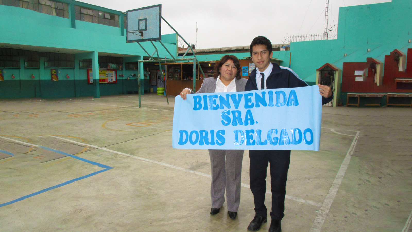 Doris mostrando un pancarta que dice Bienvenida Señora dD, en un colegio.